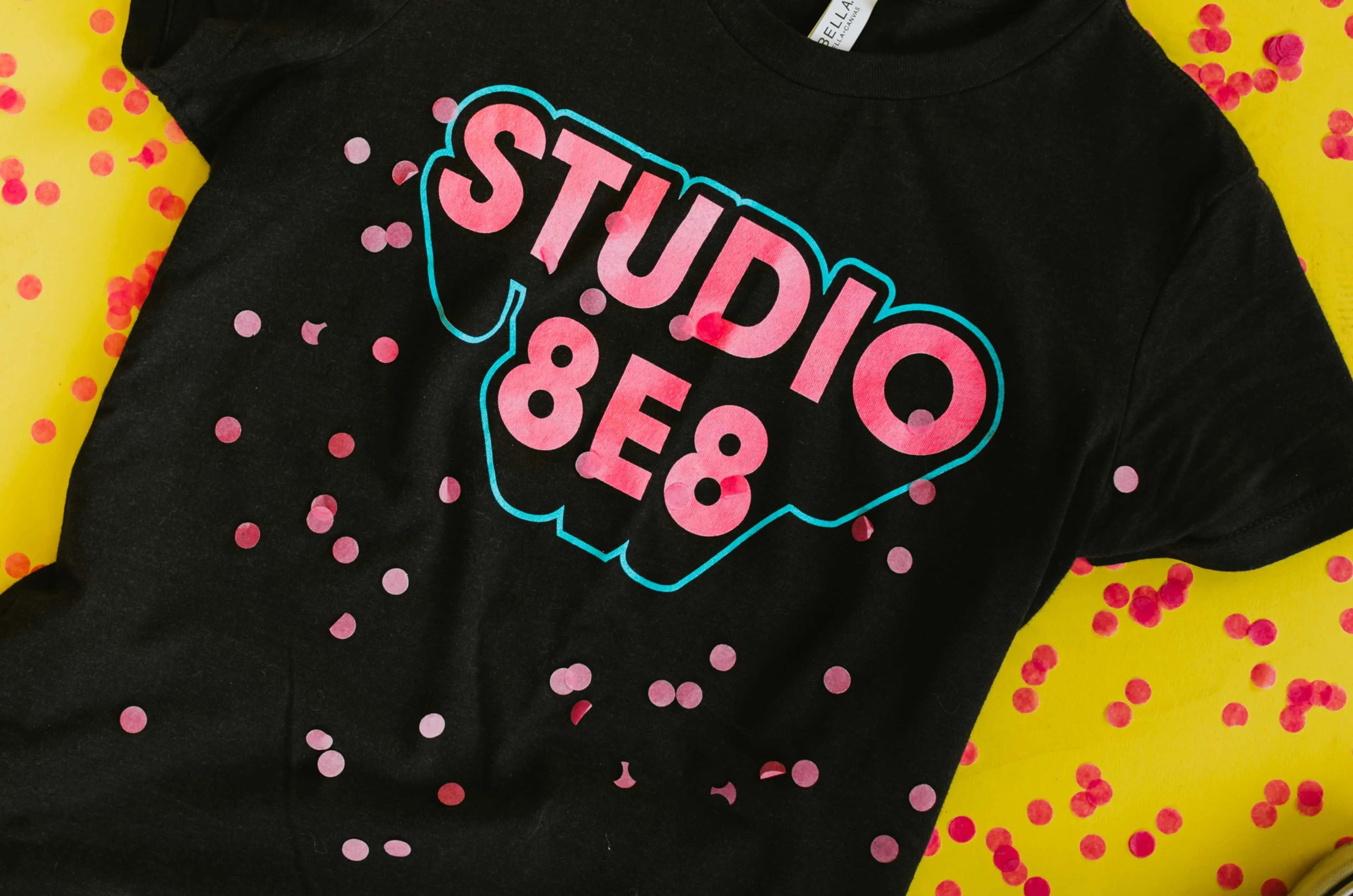Photo of a dark gray shirt with Studio 8E8 printed on it in pink letters with a blue outline
