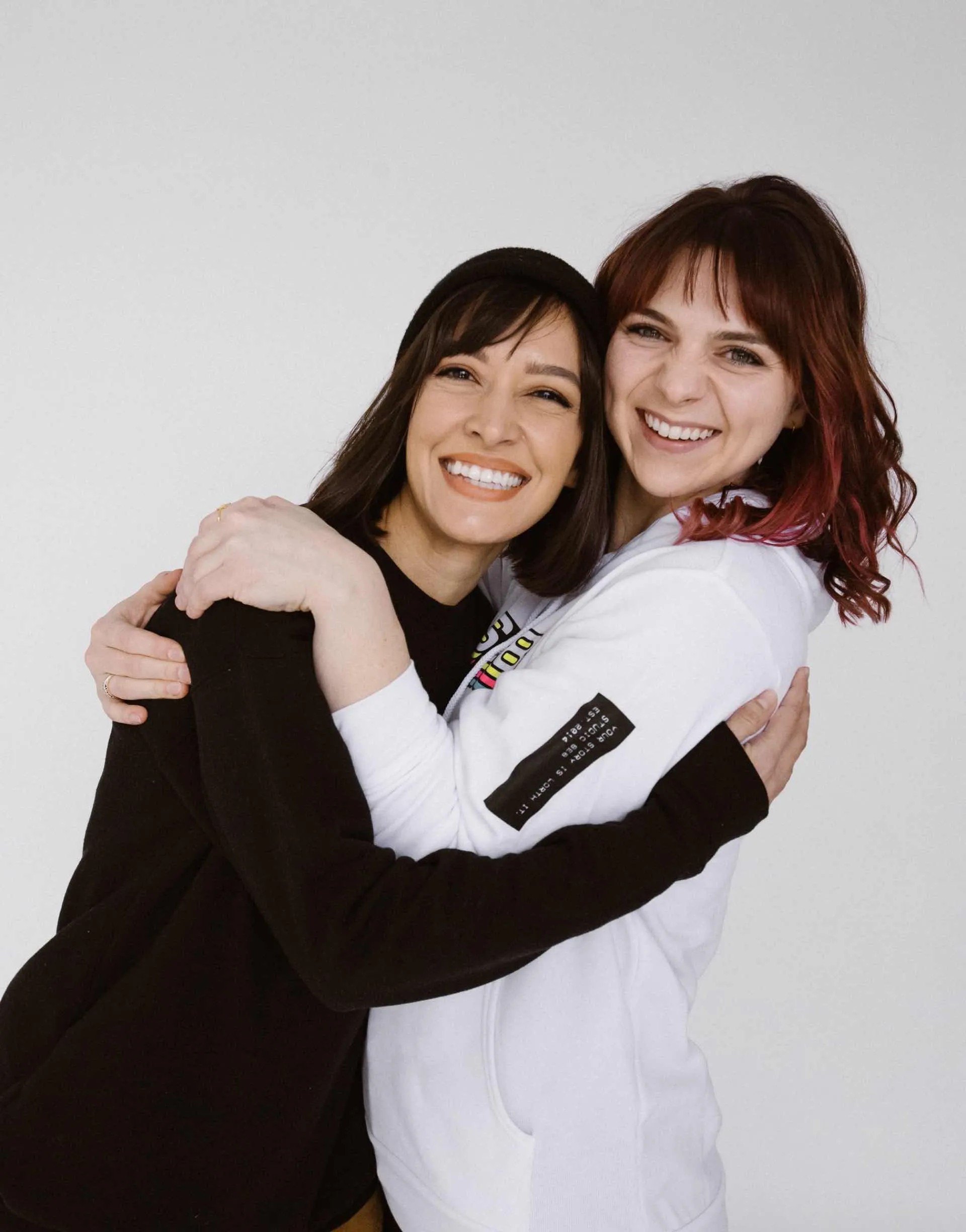 Photo of two team members hugging, wearing Studio 8E8 sweatshirts