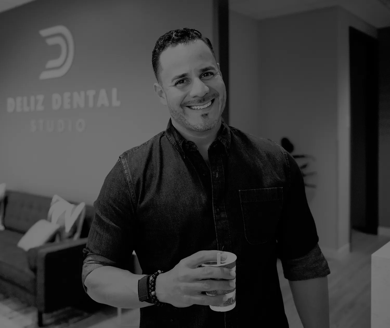 A smiling man holding a cup, standing in an office with the "Deliz Dental Studio" logo in the background, showcasing dental marketing. The image is in black and white.